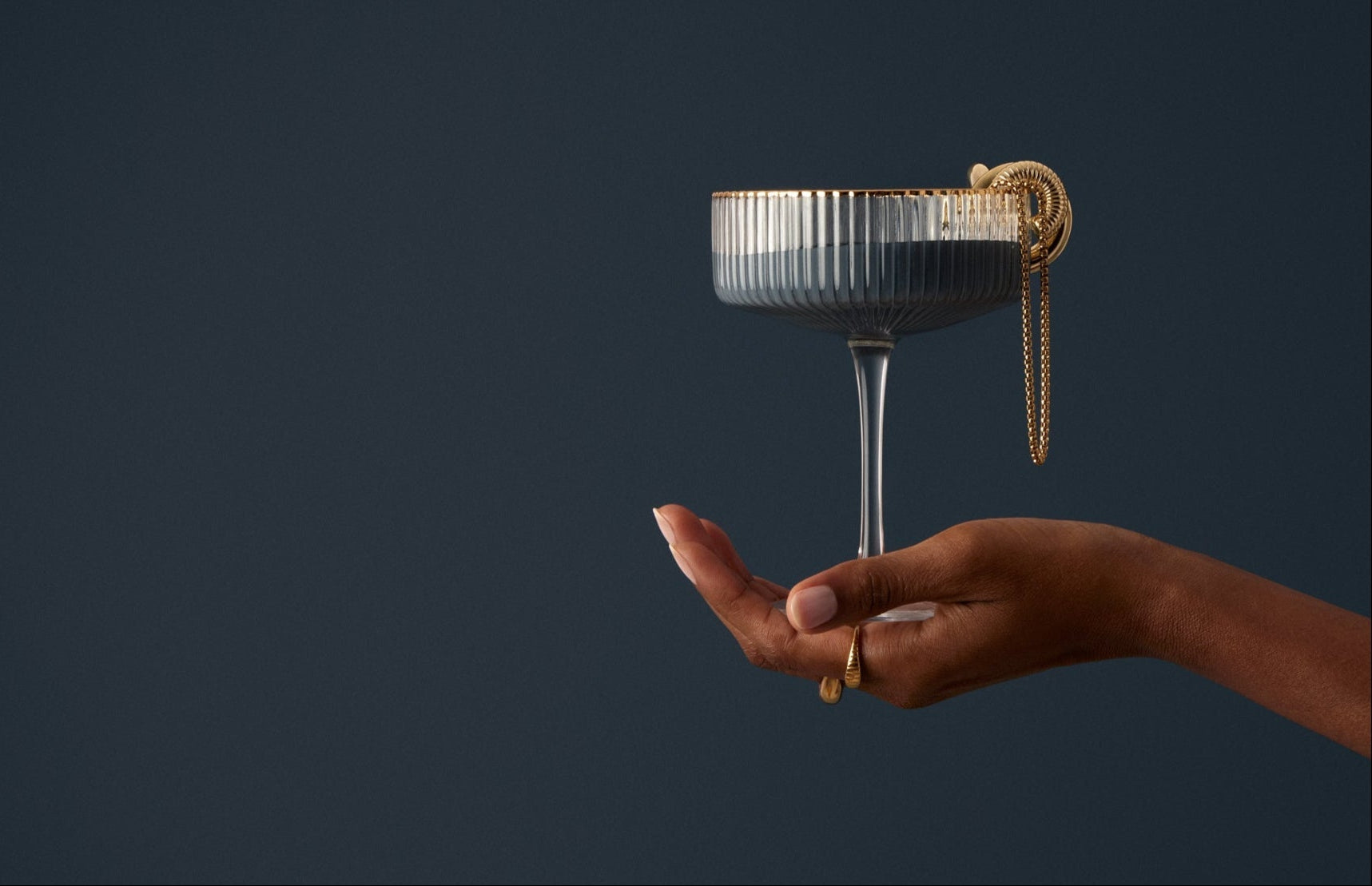 Hand holding a decorative cocktail glass against a dark background
