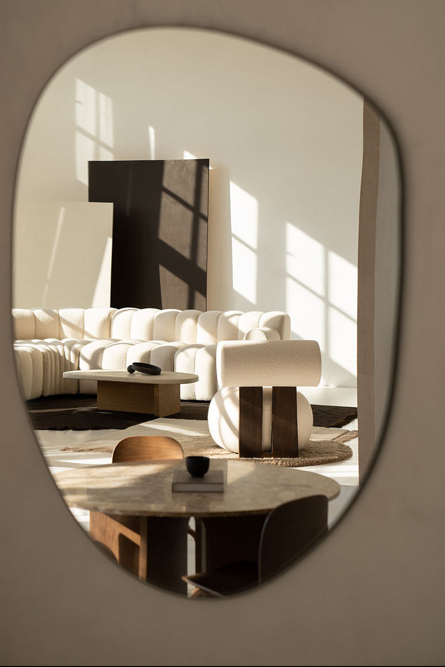 Oval mirror reflecting a modern living room with a sofa and coffee table.